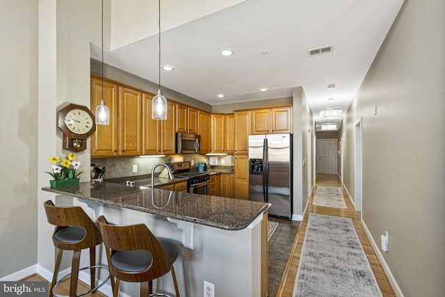 kitchen with hanging light fixtures, stainless steel appliances, a kitchen breakfast bar, kitchen peninsula, and dark stone countertops