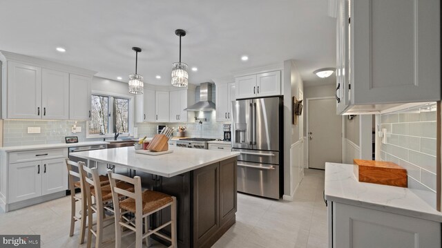 kitchen with wall chimney exhaust hood, stainless steel appliances, a kitchen island, decorative backsplash, and white cabinets