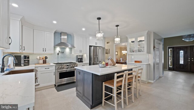 kitchen featuring appliances with stainless steel finishes, a breakfast bar, sink, wall chimney range hood, and white cabinets