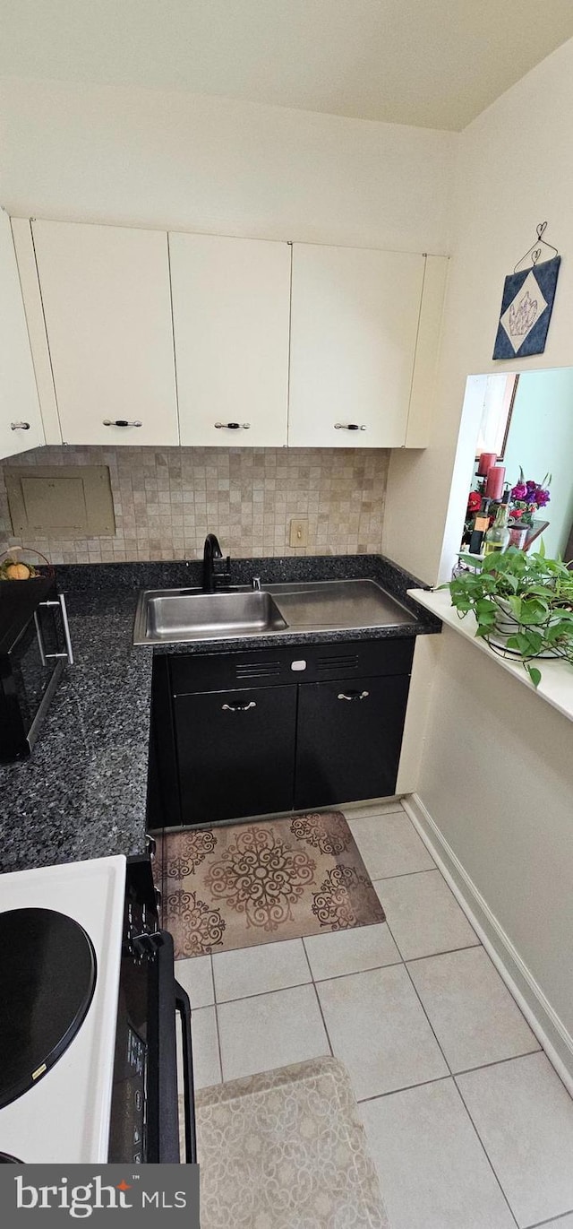 kitchen featuring backsplash, sink, light tile patterned floors, range, and white cabinetry