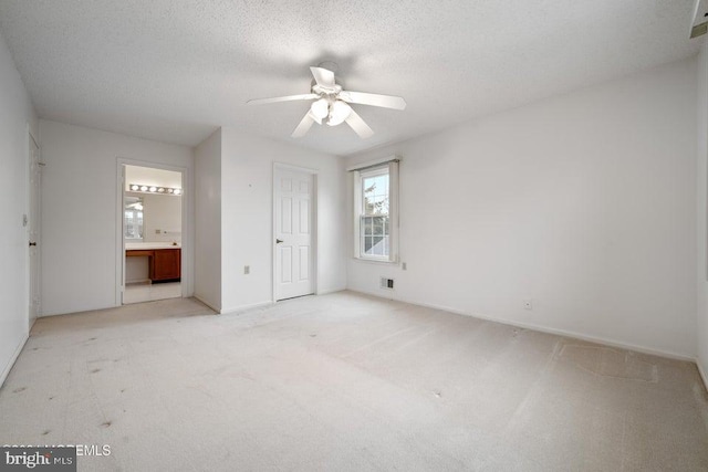 unfurnished bedroom featuring light carpet, a textured ceiling, ensuite bathroom, and ceiling fan