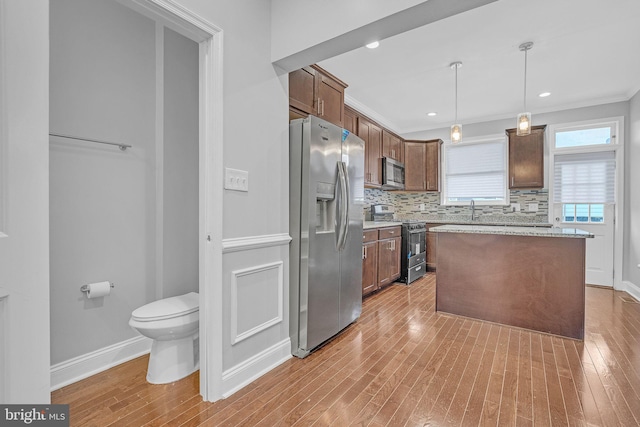 kitchen with a center island, hanging light fixtures, stainless steel appliances, backsplash, and light wood-type flooring