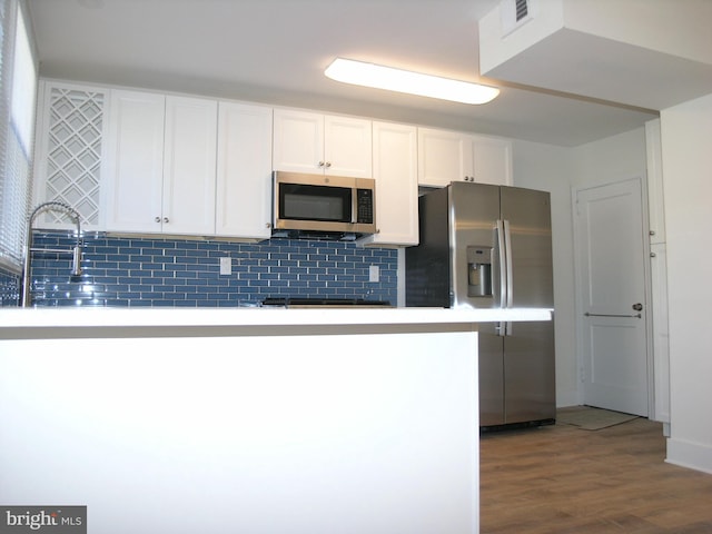 kitchen with white cabinets, wood-type flooring, appliances with stainless steel finishes, and tasteful backsplash