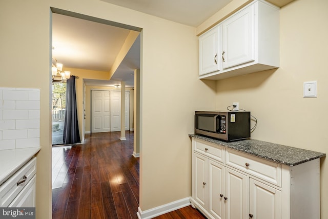 kitchen with dark hardwood / wood-style flooring, white cabinets, dark stone counters, and an inviting chandelier