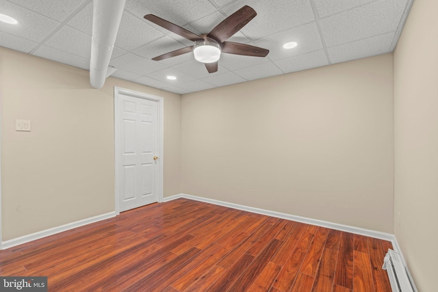 empty room with dark wood-type flooring, a drop ceiling, and a baseboard heating unit