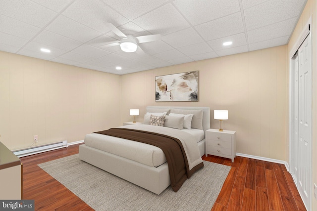 bedroom featuring a drop ceiling, baseboard heating, ceiling fan, dark hardwood / wood-style floors, and a closet