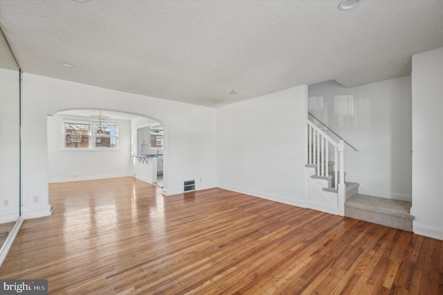 unfurnished living room with light hardwood / wood-style floors, a textured ceiling, and a chandelier