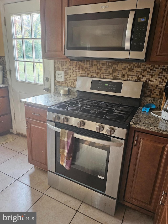 kitchen with dark stone counters, decorative backsplash, light tile patterned floors, and stainless steel appliances