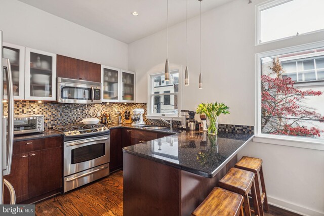 kitchen with a breakfast bar, appliances with stainless steel finishes, dark stone countertops, decorative light fixtures, and kitchen peninsula