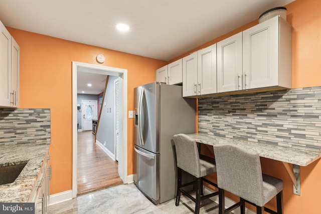 kitchen with white cabinetry, stainless steel fridge with ice dispenser, a breakfast bar, and light stone counters