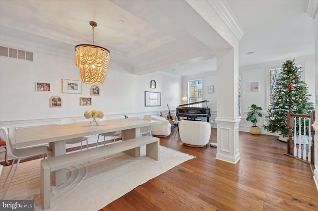 dining space with ornate columns, wood-type flooring, crown molding, and an inviting chandelier