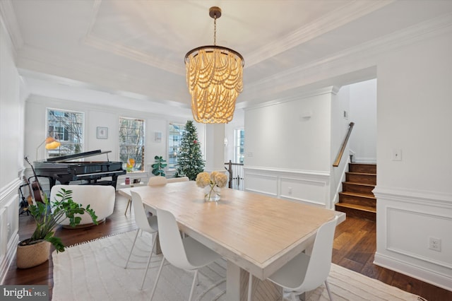 dining room featuring a raised ceiling, ornamental molding, dark wood-type flooring, and an inviting chandelier