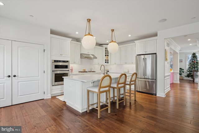 kitchen featuring pendant lighting, a kitchen island with sink, dark wood-type flooring, white cabinetry, and stainless steel appliances