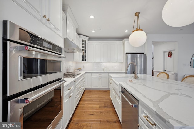 kitchen featuring pendant lighting, white cabinets, light hardwood / wood-style flooring, light stone countertops, and stainless steel appliances