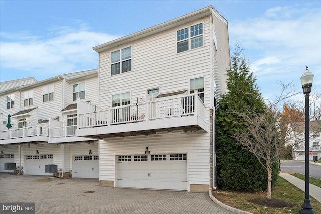 rear view of house featuring a balcony, a garage, and central air condition unit