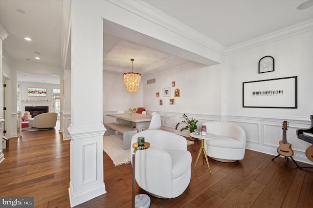 living area with ornamental molding, decorative columns, an inviting chandelier, and dark wood-type flooring