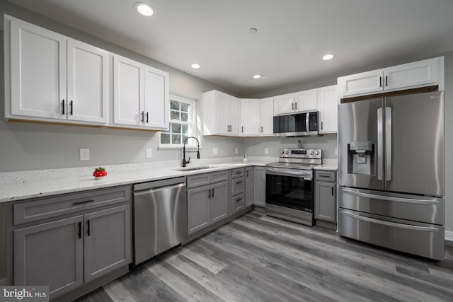 kitchen with appliances with stainless steel finishes, sink, light stone counters, white cabinets, and gray cabinets