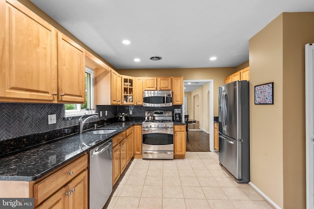 kitchen with sink, tasteful backsplash, light tile patterned floors, dark stone countertops, and appliances with stainless steel finishes