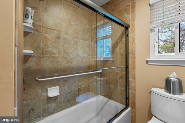 bathroom featuring toilet and bath / shower combo with glass door