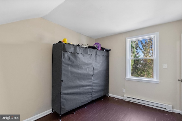 empty room featuring dark hardwood / wood-style flooring, a baseboard radiator, and vaulted ceiling