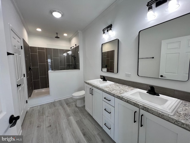 bathroom featuring vanity, crown molding, tiled shower, wood-type flooring, and toilet