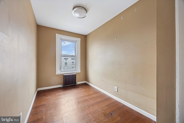 empty room featuring radiator heating unit, hardwood / wood-style flooring, and baseboards