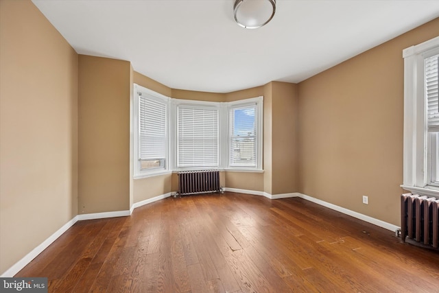 empty room featuring baseboards, wood finished floors, and radiator