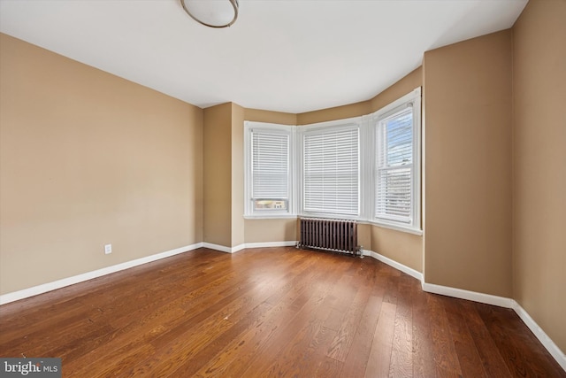 spare room with radiator heating unit, wood-type flooring, and baseboards