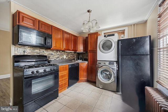 kitchen featuring stacked washer / dryer, backsplash, black appliances, radiator heating unit, and an inviting chandelier