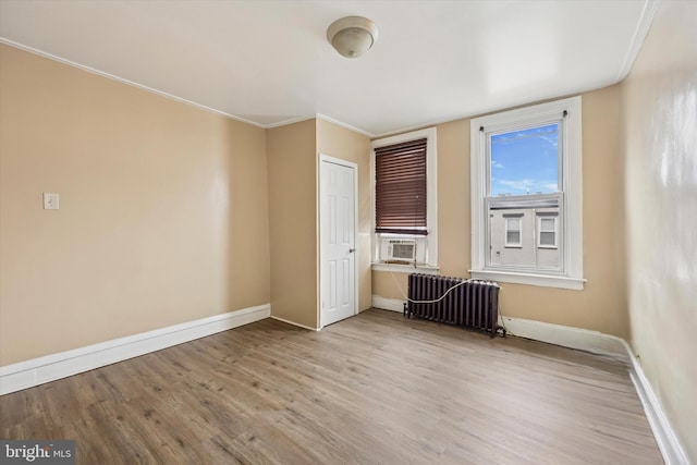 unfurnished bedroom featuring radiator, baseboards, wood finished floors, and ornamental molding