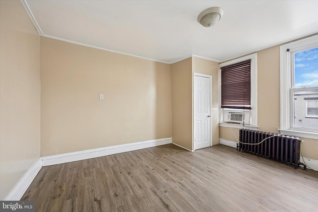 spare room featuring radiator, baseboards, wood finished floors, and ornamental molding