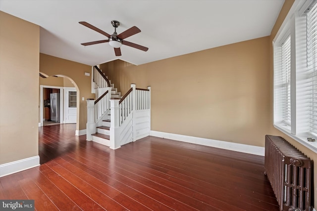 spare room with arched walkways, hardwood / wood-style flooring, baseboards, stairs, and radiator