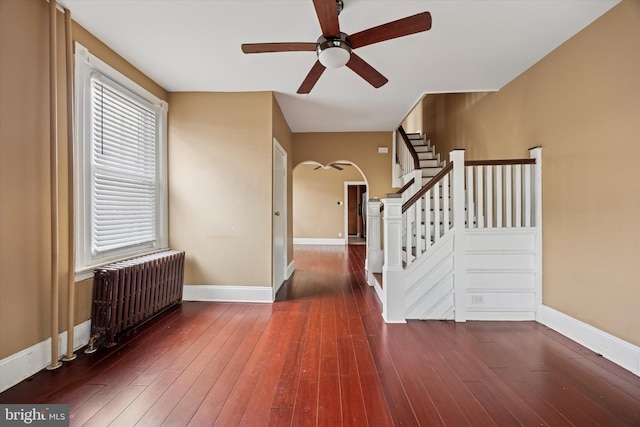 entrance foyer featuring arched walkways, baseboards, stairs, radiator heating unit, and wood-type flooring