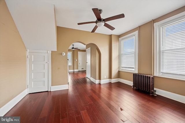 unfurnished room with hardwood / wood-style flooring, radiator heating unit, arched walkways, and baseboards