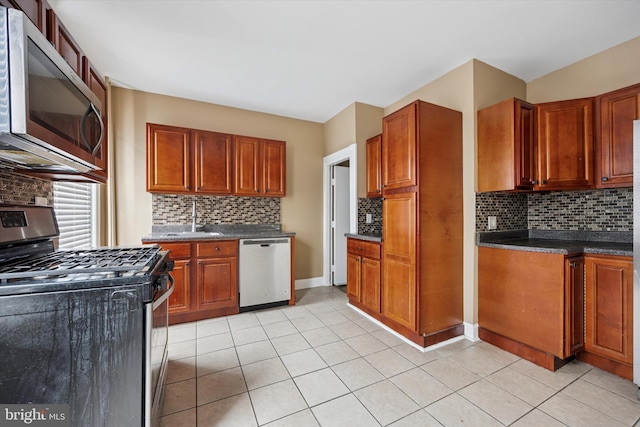 kitchen with light tile patterned floors, stainless steel appliances, a sink, decorative backsplash, and dark countertops