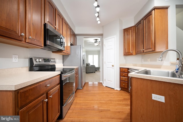 kitchen with rail lighting, sink, ceiling fan, appliances with stainless steel finishes, and light hardwood / wood-style floors