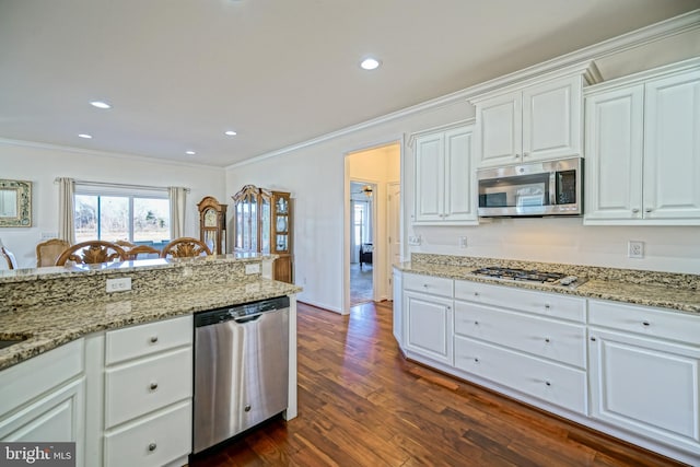 kitchen featuring dark wood-type flooring, white cabinetry, stainless steel appliances, light stone counters, and ornamental molding