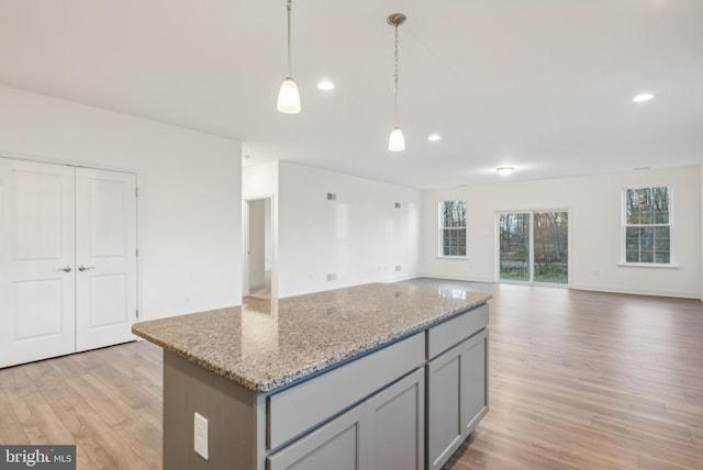 kitchen featuring light stone countertops, light wood-type flooring, pendant lighting, gray cabinets, and a kitchen island