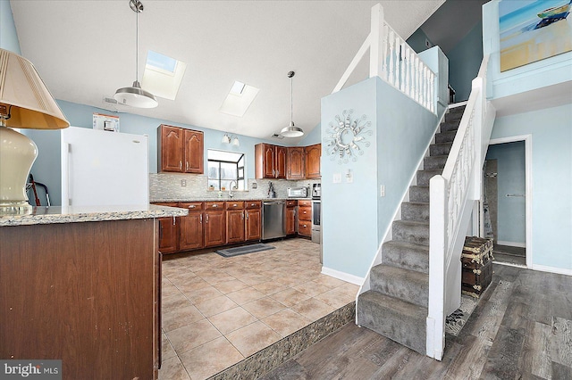 kitchen featuring a skylight, hanging light fixtures, light stone counters, stainless steel dishwasher, and light hardwood / wood-style floors