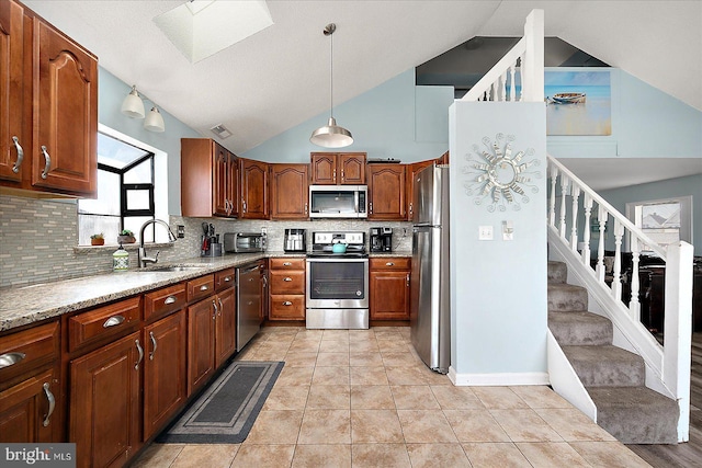 kitchen with sink, light stone countertops, appliances with stainless steel finishes, tasteful backsplash, and decorative light fixtures