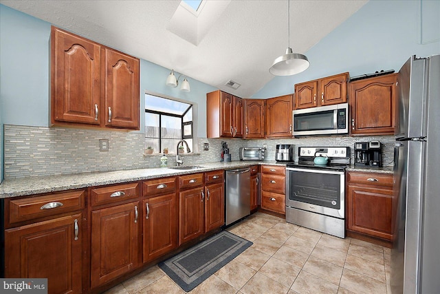 kitchen with pendant lighting, lofted ceiling with skylight, sink, appliances with stainless steel finishes, and light stone counters