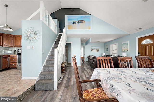 dining room with wood-type flooring, a textured ceiling, and high vaulted ceiling