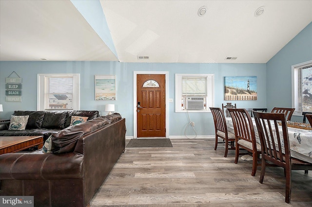 living room with plenty of natural light, cooling unit, vaulted ceiling, and light wood-type flooring