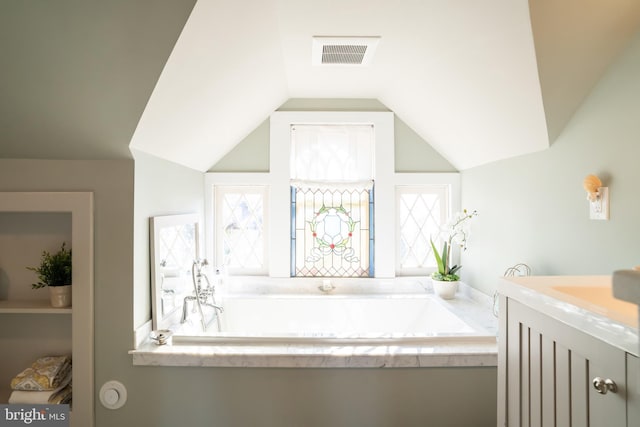 bathroom featuring a relaxing tiled tub, lofted ceiling, and vanity