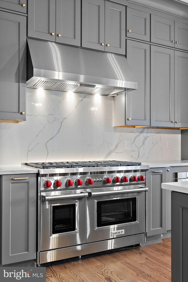 kitchen featuring backsplash, gray cabinets, light hardwood / wood-style floors, and range with two ovens