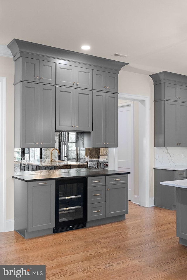 bar featuring gray cabinetry, decorative backsplash, light wood-type flooring, and beverage cooler