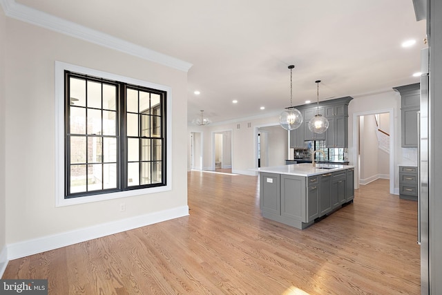 kitchen with gray cabinetry, a center island with sink, hanging light fixtures, and light wood-type flooring