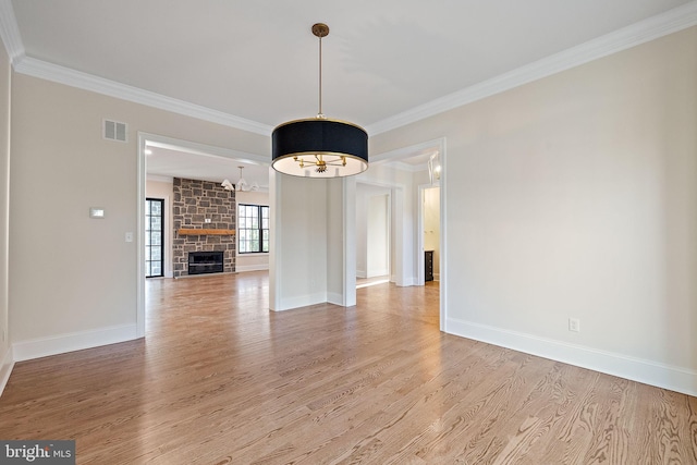 interior space featuring light hardwood / wood-style floors, a stone fireplace, ornamental molding, and a chandelier