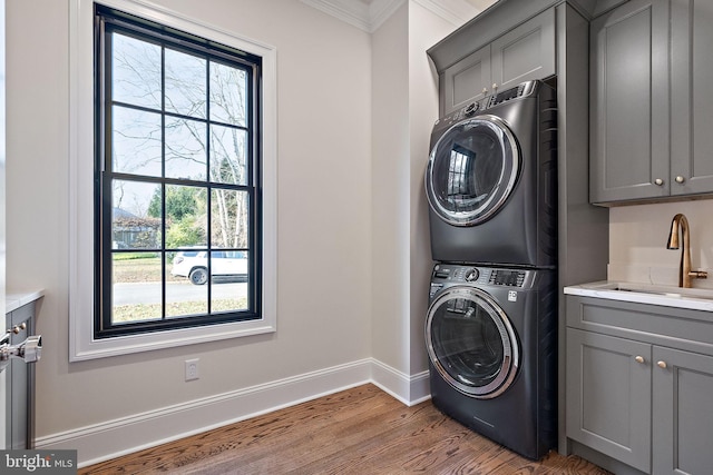 laundry room featuring sink, cabinets, stacked washing maching and dryer, crown molding, and light wood-type flooring