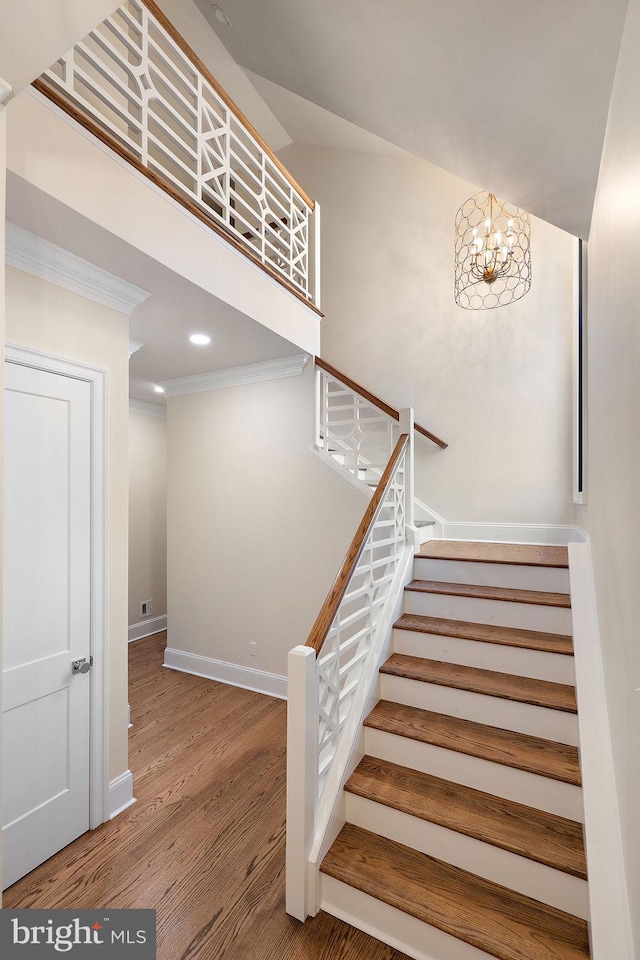 stairs with hardwood / wood-style flooring, crown molding, and a chandelier